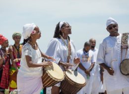 Men and women dressed in white and African attire drumming.